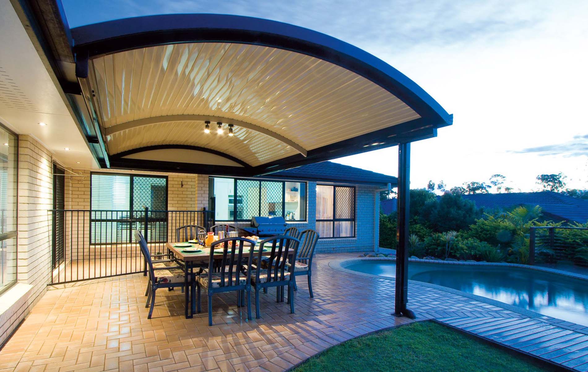 Curved patio with dining set beside a pool and ambient garden lighting