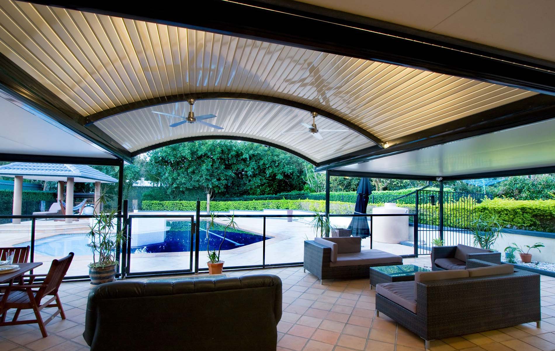 Modern curved patio design with polycarbonate roofing and leafy backdrop