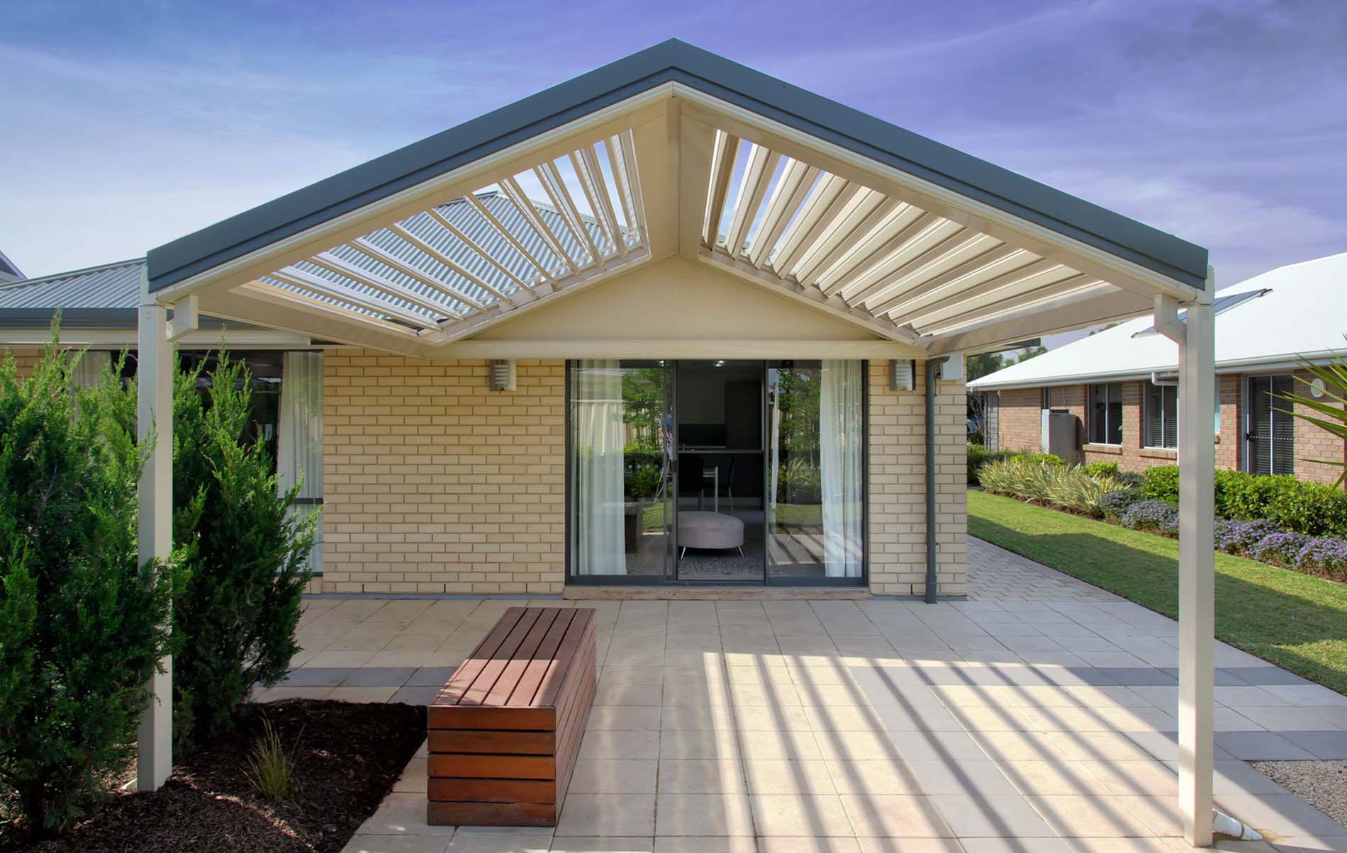 Open louvre patio with adjustable slats over paved area, timber bench and garden view