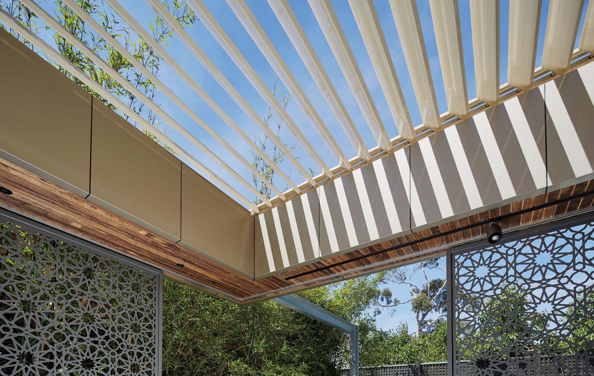 Close‑up of louvre patio roof with adjustable slats casting shadow pattern over timber frame and decorative screen