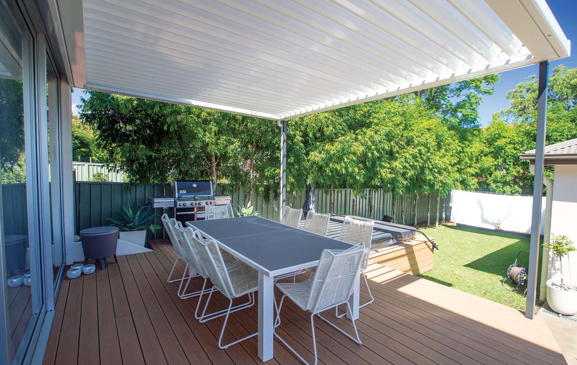 Outdoor dining area under white louvre roof with garden view and timber decking