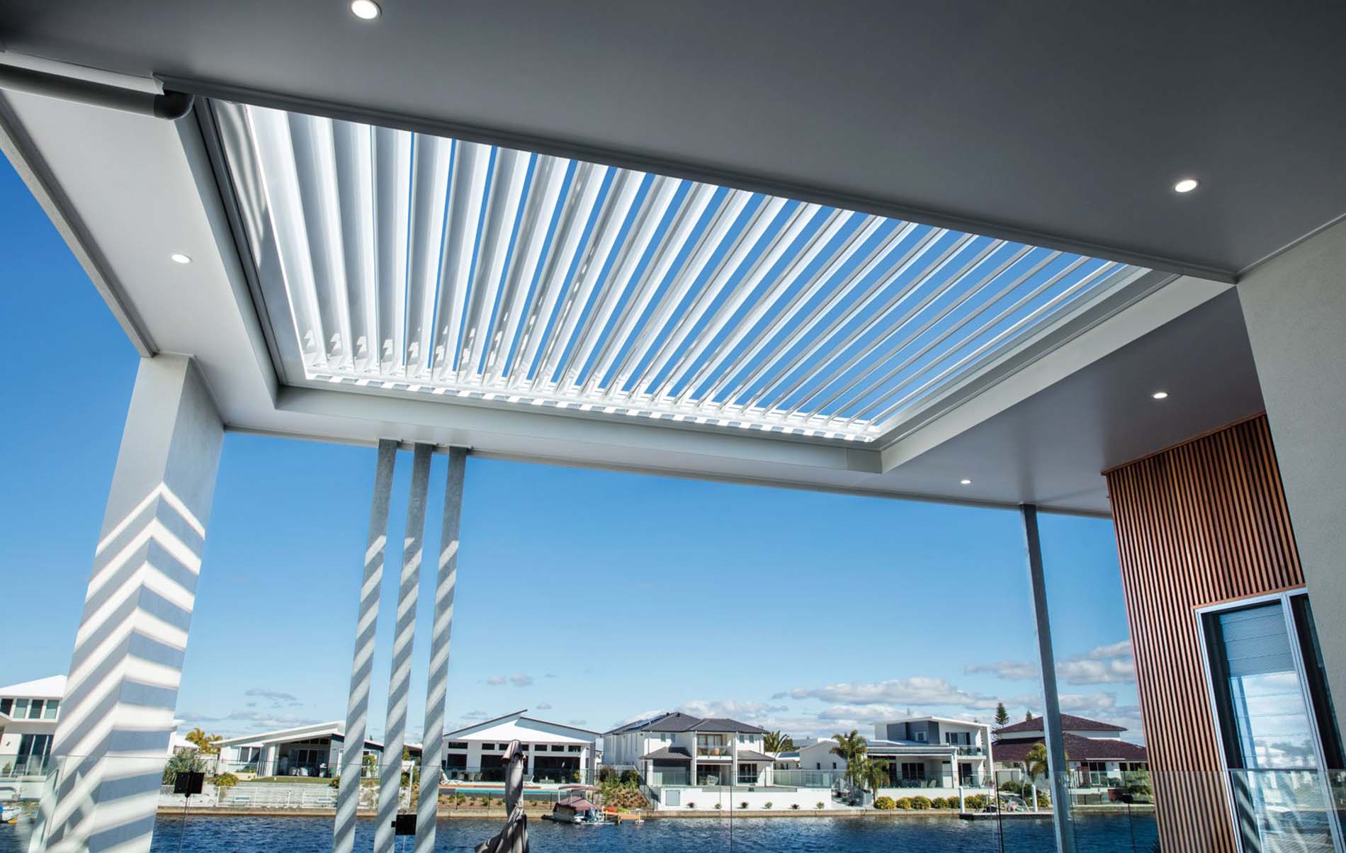 Outdoor lounge area beneath adjustable louvre roof with integrated lighting and timber-look frame