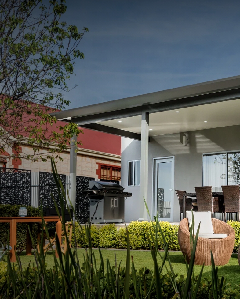 Covered patio with seating, greenery and grill attached to home