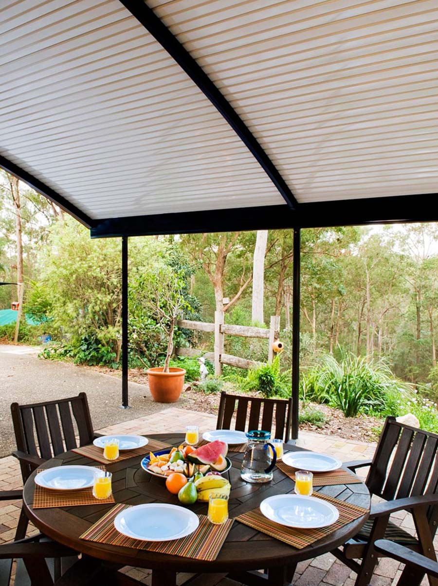 Curved patio roof covering round dining table with breakfast setting outdoors